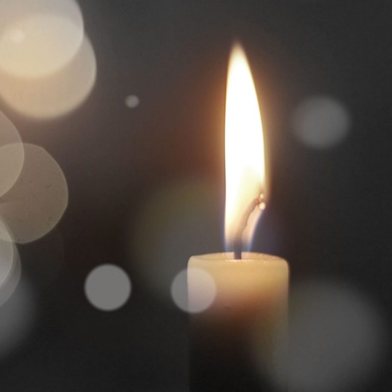 Eine brennende Kerze mit warmem Licht vor einem dunklen, unscharfen Hintergrund.