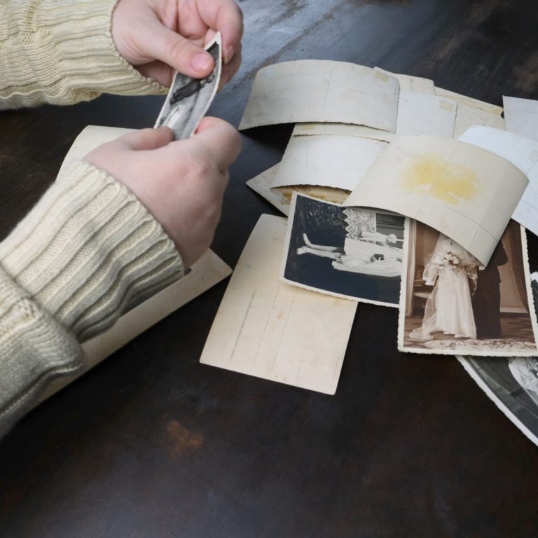 Eine Hand hält ein Foto über einer Sammlung alter Schwarz-Weiß-Fotos auf einem Tisch.